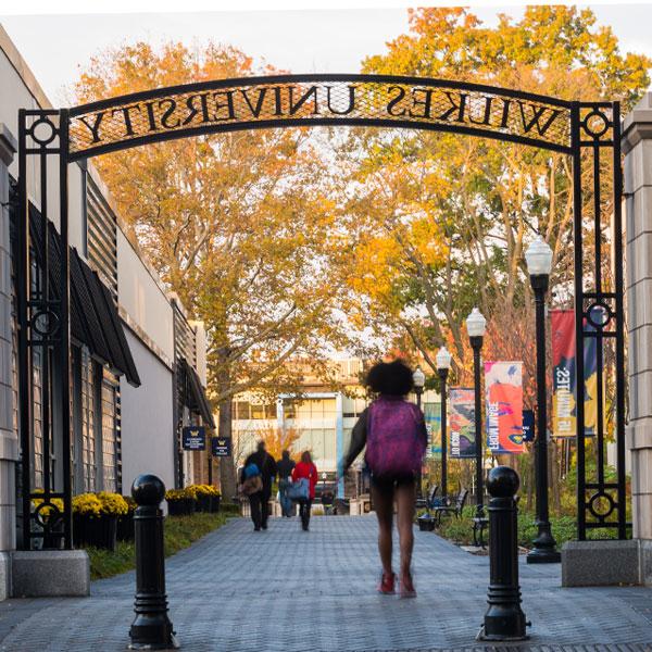 Wilkes student walking under campus gateway